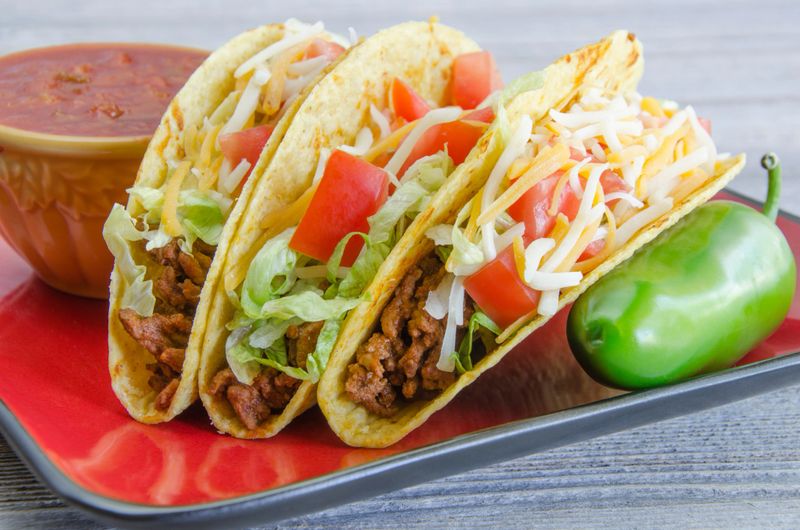 "A plate of tacos made with lettuce, tomatoes, cheese and ground beef.  On a red plate with salsa and a green pepper.Similar Images:"