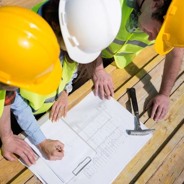 Construction workers in hard hats reviewing building blueprints on wooden planks.