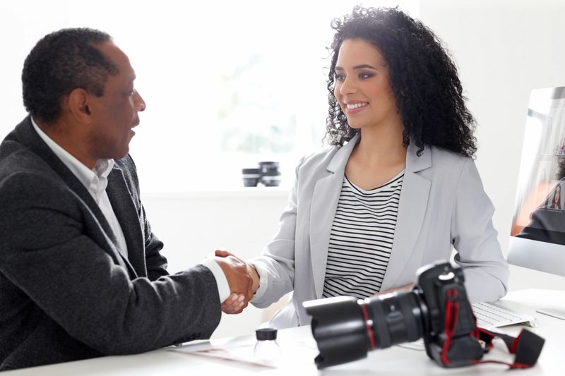 Pretty young female photographer shaking hands with client at her desk