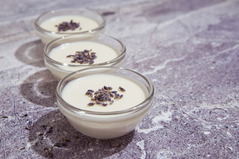 Lavender panna cota in transparent bowls on the stone background. Tasty and delicious Italian dessert with dry levender. Three small bowls of milk pudding or cream jelly.