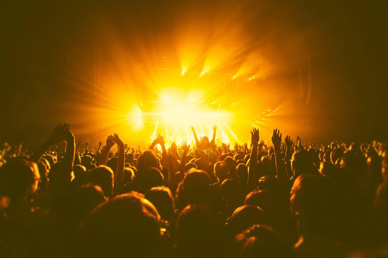 A crowded concert hall with scene stage orange and yellow lights, rock show performance