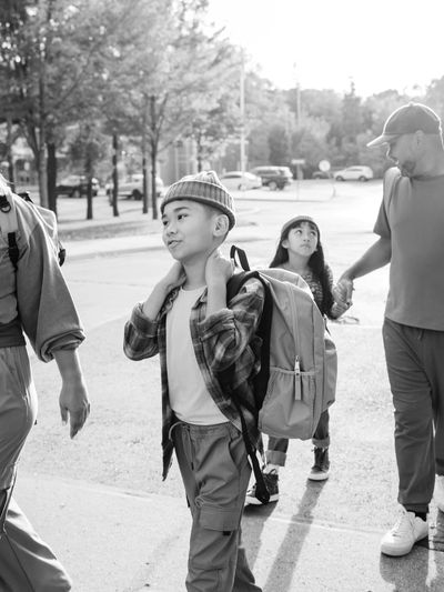 A family walking outdoors on a sunny day, carrying backpacks and chatting.