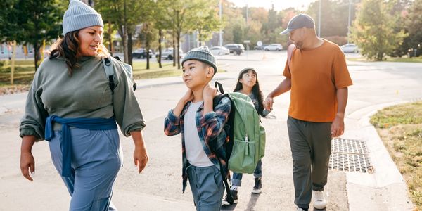 A family walking outdoors on a sunny day, carrying backpacks and chatting.