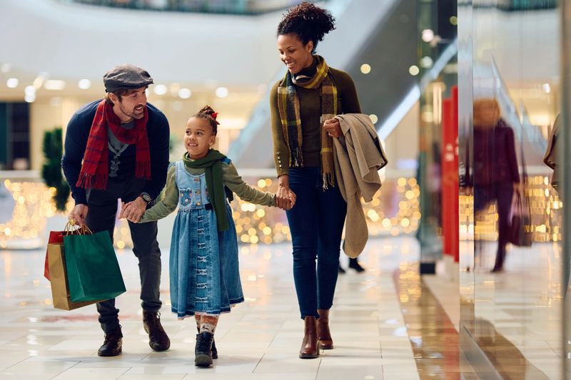 Happy parents and their daughter holding hands during Christmas shopping at the mall. Copy space.