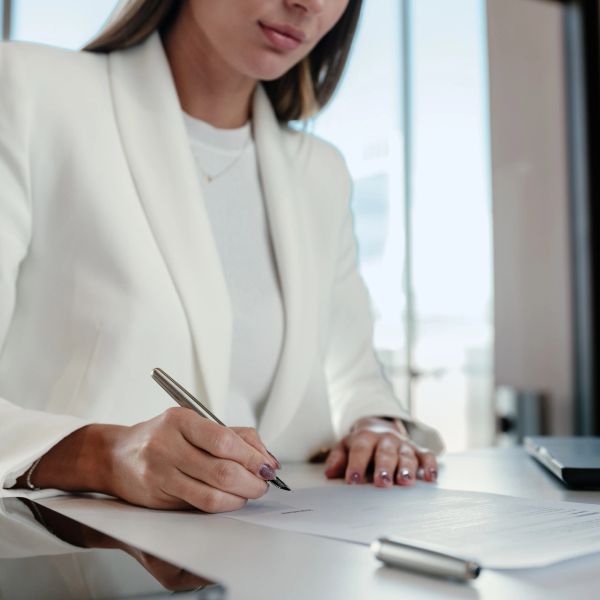 Person in white suit signing a document at a desk.
