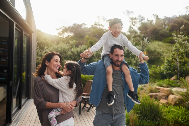 Smiling parents carrying their two adorable young children outside on their patio at home in the summertime