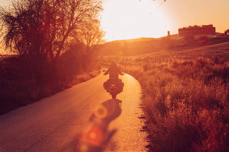 Lone motorcyclist riding his motorcycle into the sunset on a narrow highway
