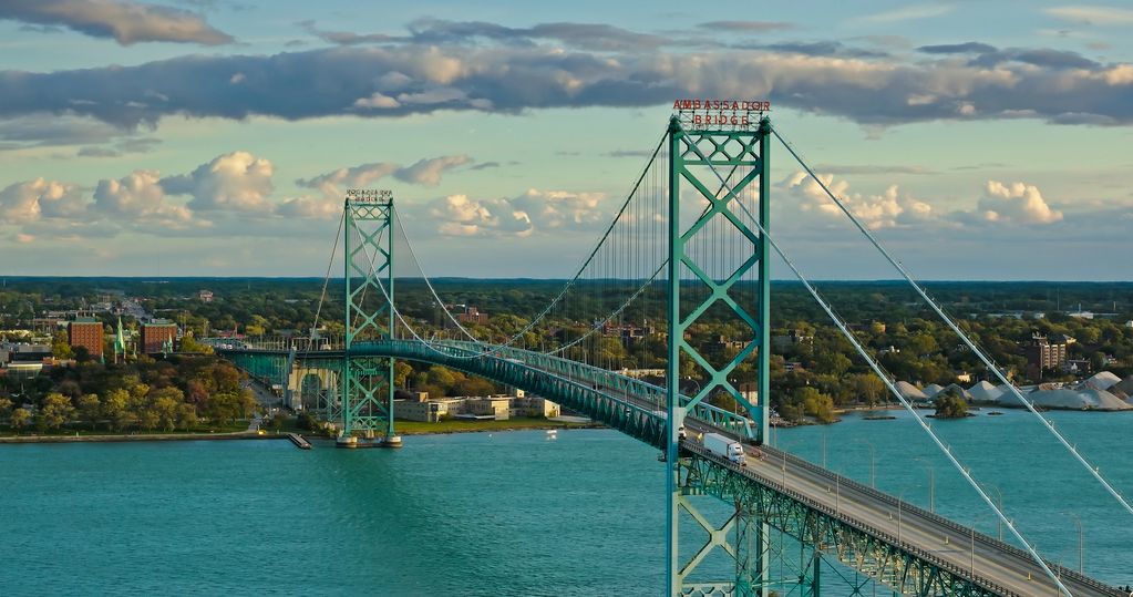 View of Ambassador Bridge spanning turquoise water under a partly cloudy sky.