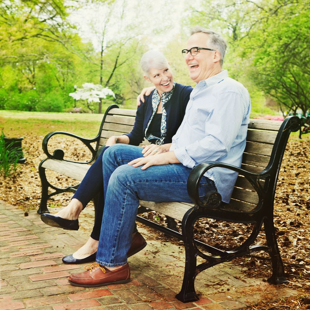 Elderly couple laughing together on a park bench.