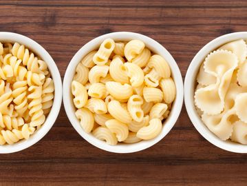 Three bowls of different types of cooked pasta on a wooden surface.