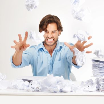 Frustrated man throwing crumpled papers in the air at his desk.