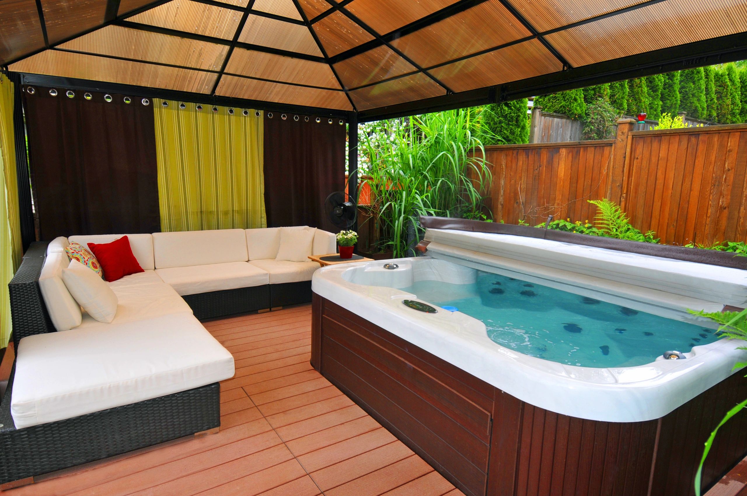 Outdoor lounge area with a hot tub and cushioned seating under a covered pergola.