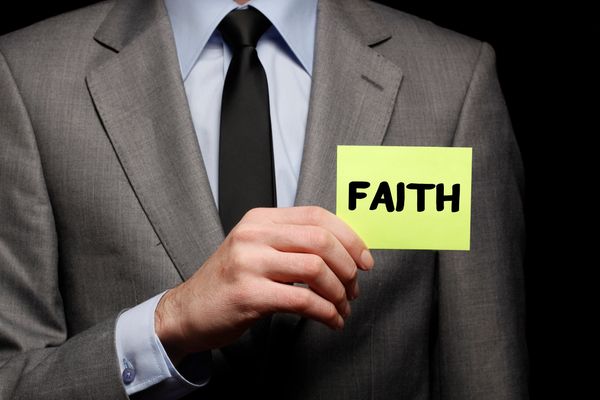Attorney in a grey suit, blue shirt, and black tie, holding up a sign that says "Faith."