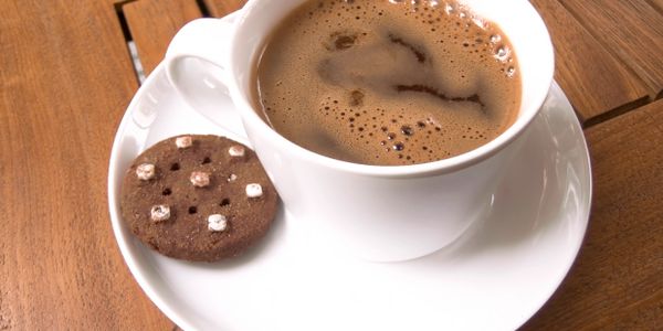 White cup of coffee with a chocolate cookie on a white saucer.