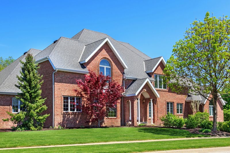 Beautiful two story red brick home nicely landscaped with blue sky in the background.