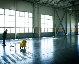 Janitor mopping an empty industrial floor.
