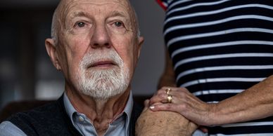 Elderly man with a thoughtful expression, supported by a comforting hand on his shoulder.