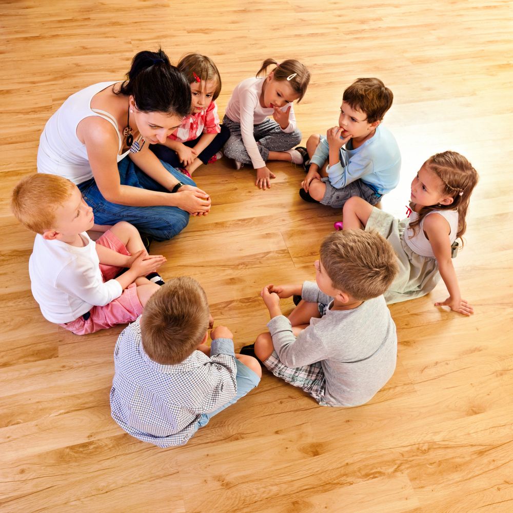 Teacher and children sitting in a circle on the floor during group activity.