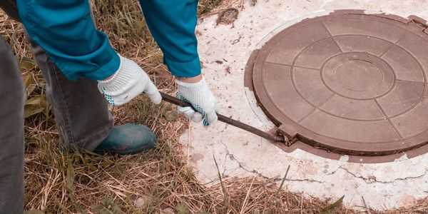 Person opening a manhole cover with a crowbar outdoors.