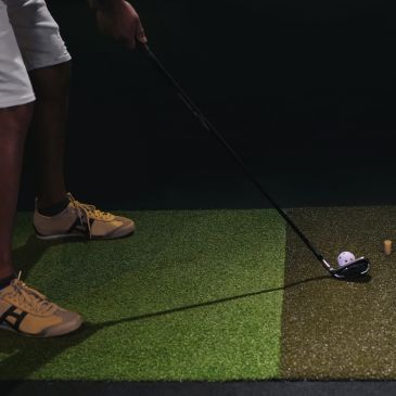 Person preparing to hit a golf ball indoors on artificial turf.