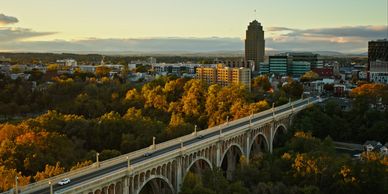 A scenic city view with a historic bridge and autumn trees at sunset.