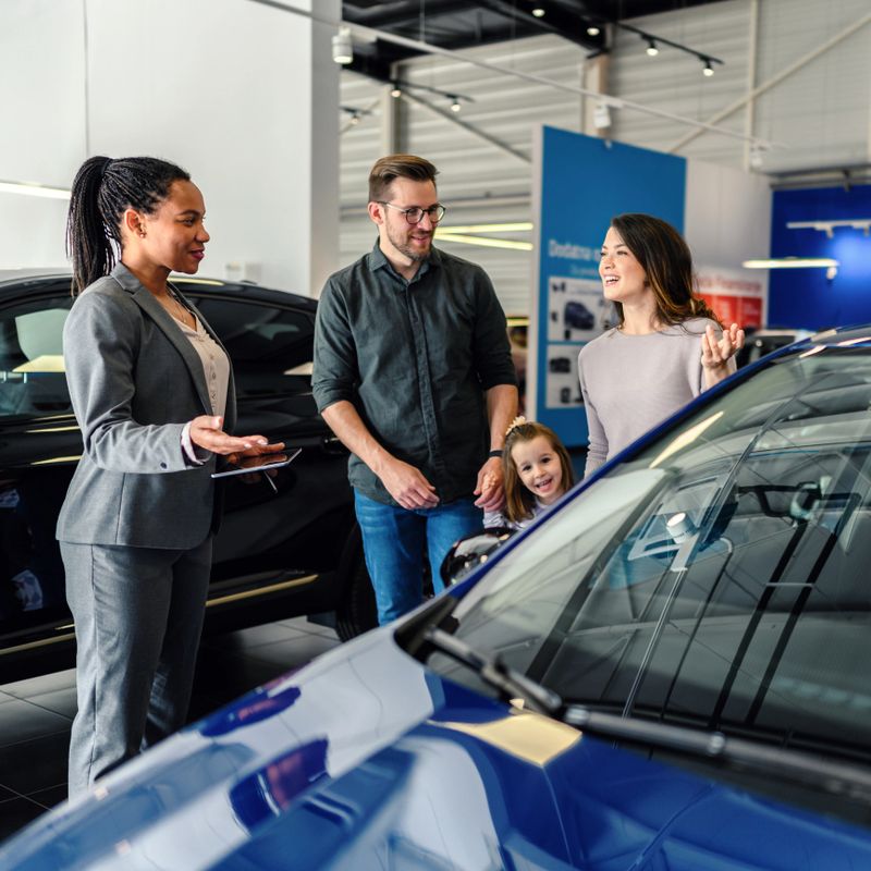 Saleswoman at car dealership center helping family to choose new family vehicle