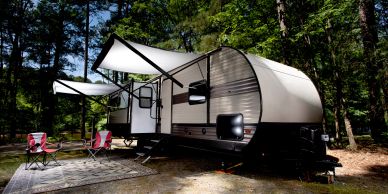 A travel trailer with awnings set up in a forested campsite.