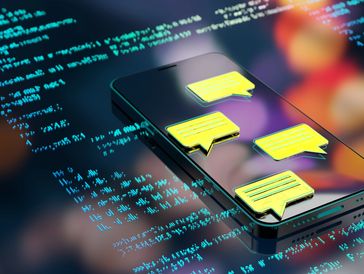 Smartphone screen with glowing yellow chat icons and floating blue code symbols.
