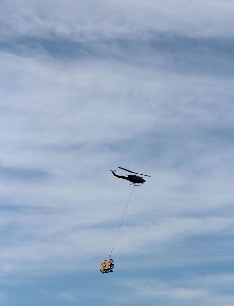 A helicopter carries a load of cargo on the end of a cable against blue sky and light clouds near Wrangell, Alaska.