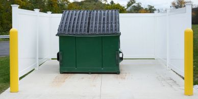 A green dumpster behind white fencing.