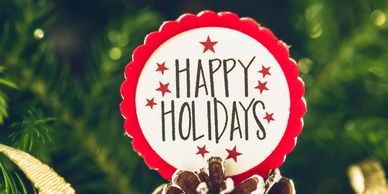 Decorative pinecone with a holiday greeting tag and golden ribbon on a green pine branch.