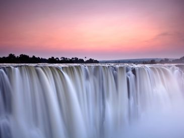 Majestic waterfall under a colorful sky at sunset.