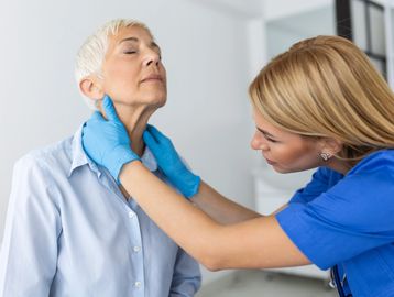 A nurse checks an elderly woman's neck with blue gloves on.