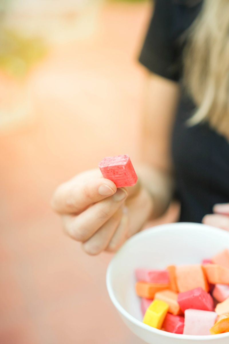 Vertical closeup view of one candy holded by unrecognizable white woman with some other candies in a white bowl