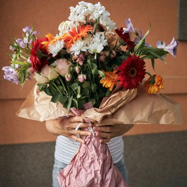 Person holding a colorful bouquet of flowers wrapped in paper.
