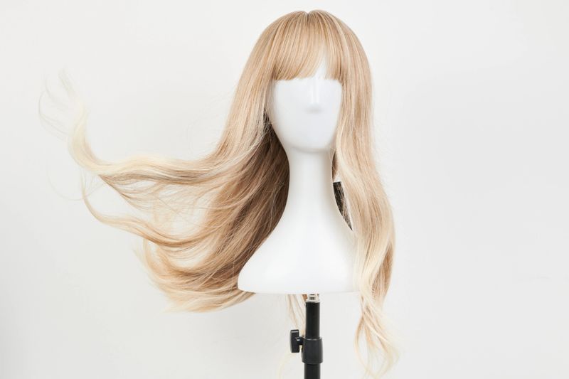Natural looking blonde wig on white mannequin head. Long hair on the plastic wig holder isolated on white background, front view