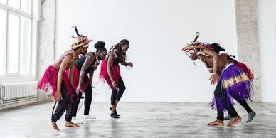 Group of people performing a traditional dance indoors wearing colorful skirts and hats.