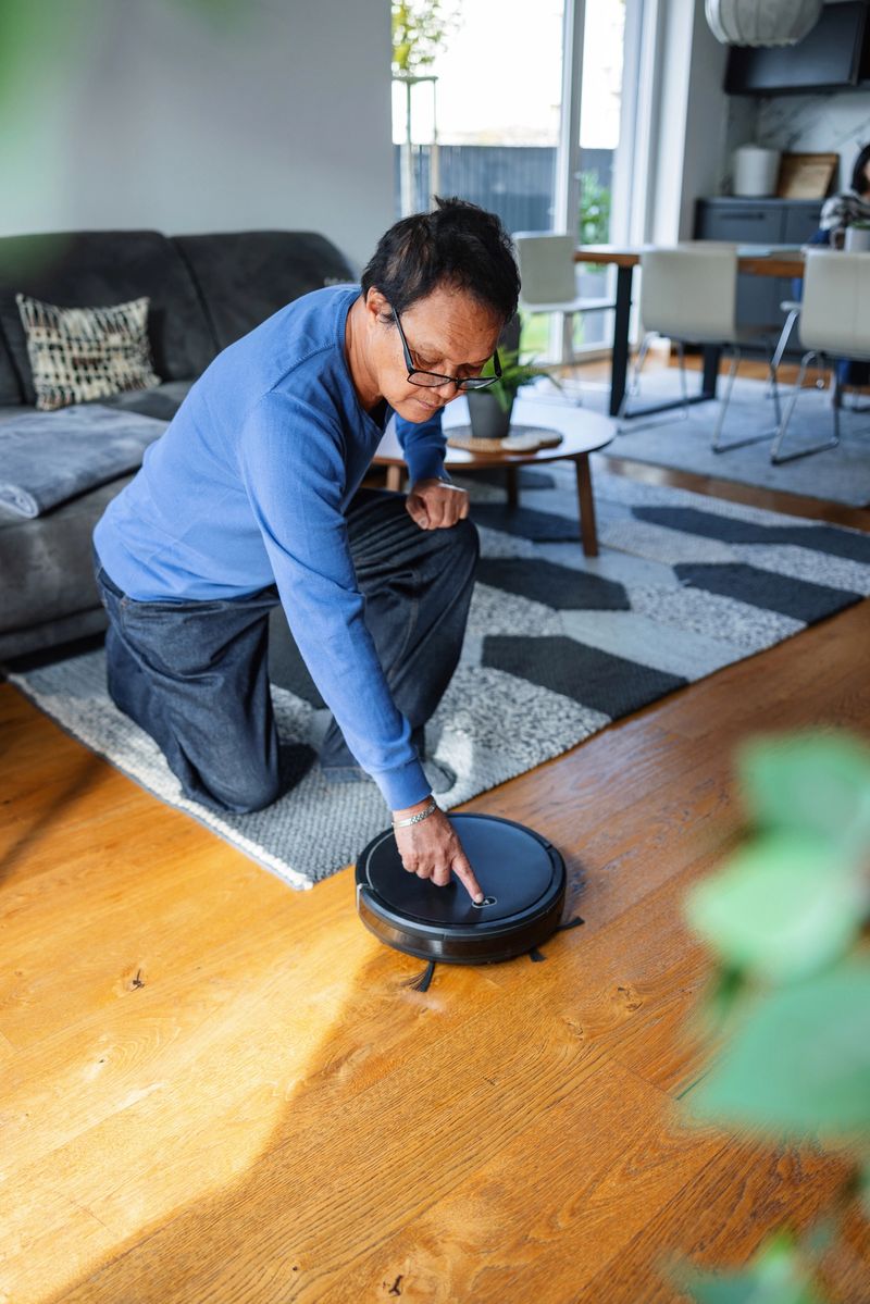 A thoughtful senior Asian man watches a robotic vacuum cleaner at work, reflecting on the convenience of modern home technology from his comfortable living room sofa.