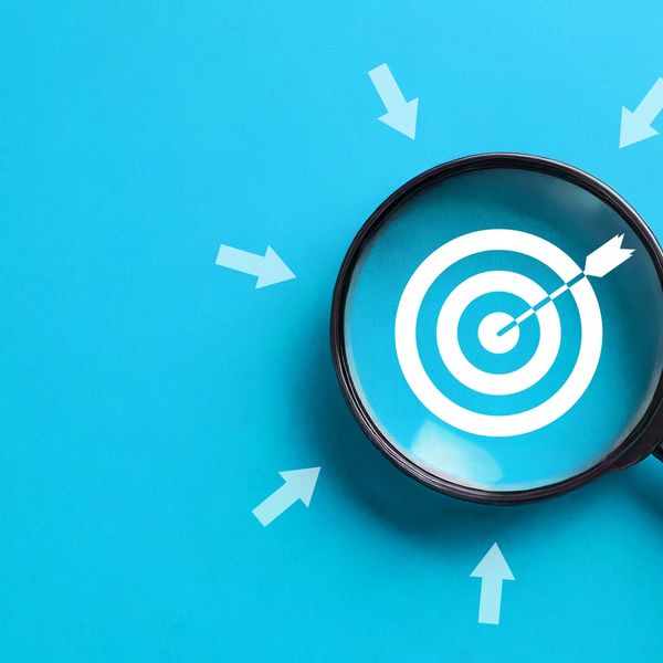 Magnifying glass focusing on a bullseye target with arrows pointing to it.