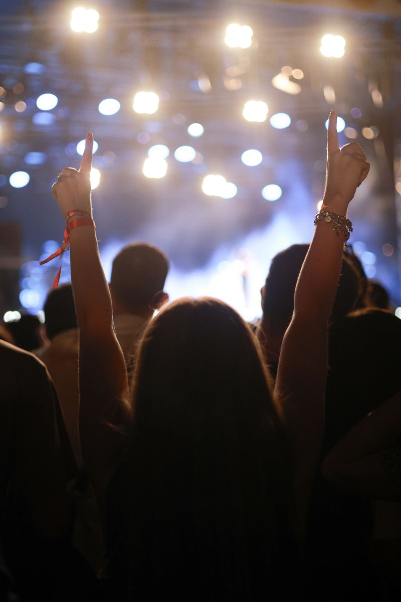Silhouette of a woman in a crowd watching concert at open air music festival and enjoying. Crowd with raised hands.