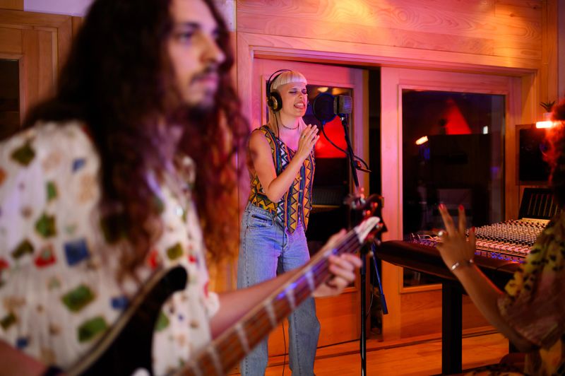 Picture of a female singer recording vocals while male bass player is performing on their string instrument. A band in a recording studio is making a new single. Selective focus on a female vocalist.