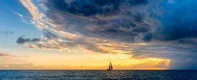 A lone sailboat on the ocean at sunset with dramatic clouds.