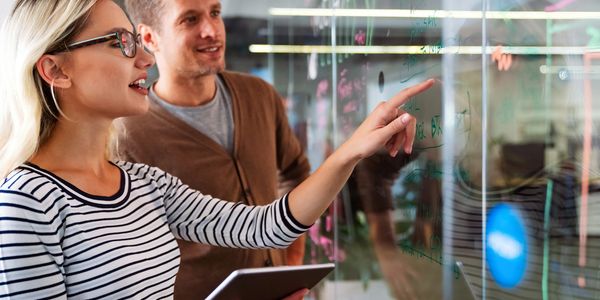 Two colleagues discussing ideas on a transparent whiteboard.
