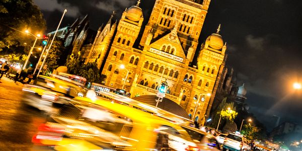 Historic building illuminated at night with busy traffic and motion blur.