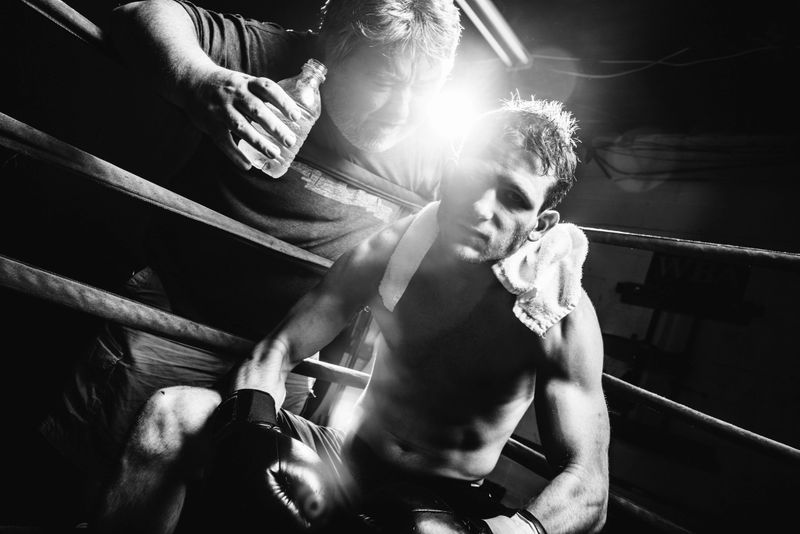 Coach encourages Boxer sitting in the boxing ring corner.