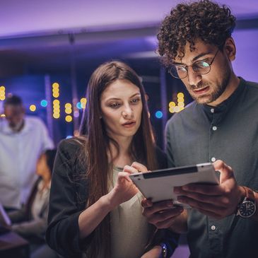 Two colleagues focused on a tablet in a modern office at night.