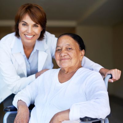 Elderly woman in wheelchair with smiling female caregiver.