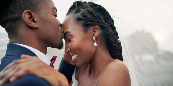 Groom tenderly kisses bride's forehead as they embrace on their wedding day.