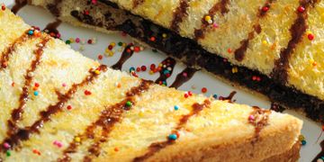 Toasted sandwich with chocolate drizzle and colorful sprinkles on a white plate.