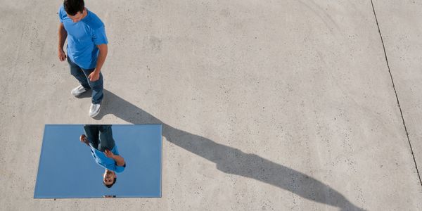 Man in blue shirt looking at his reflection in a mirror on the ground.